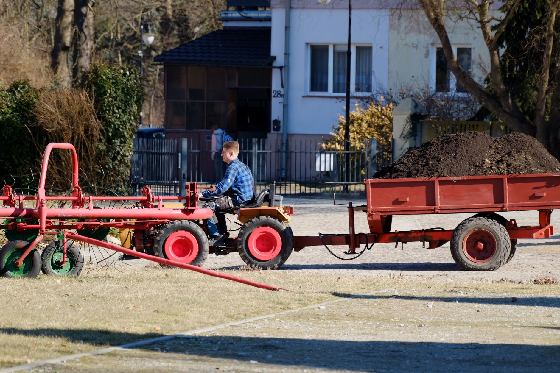 A man driving a small tractor with a trailer of soil in a residential neighborhood.