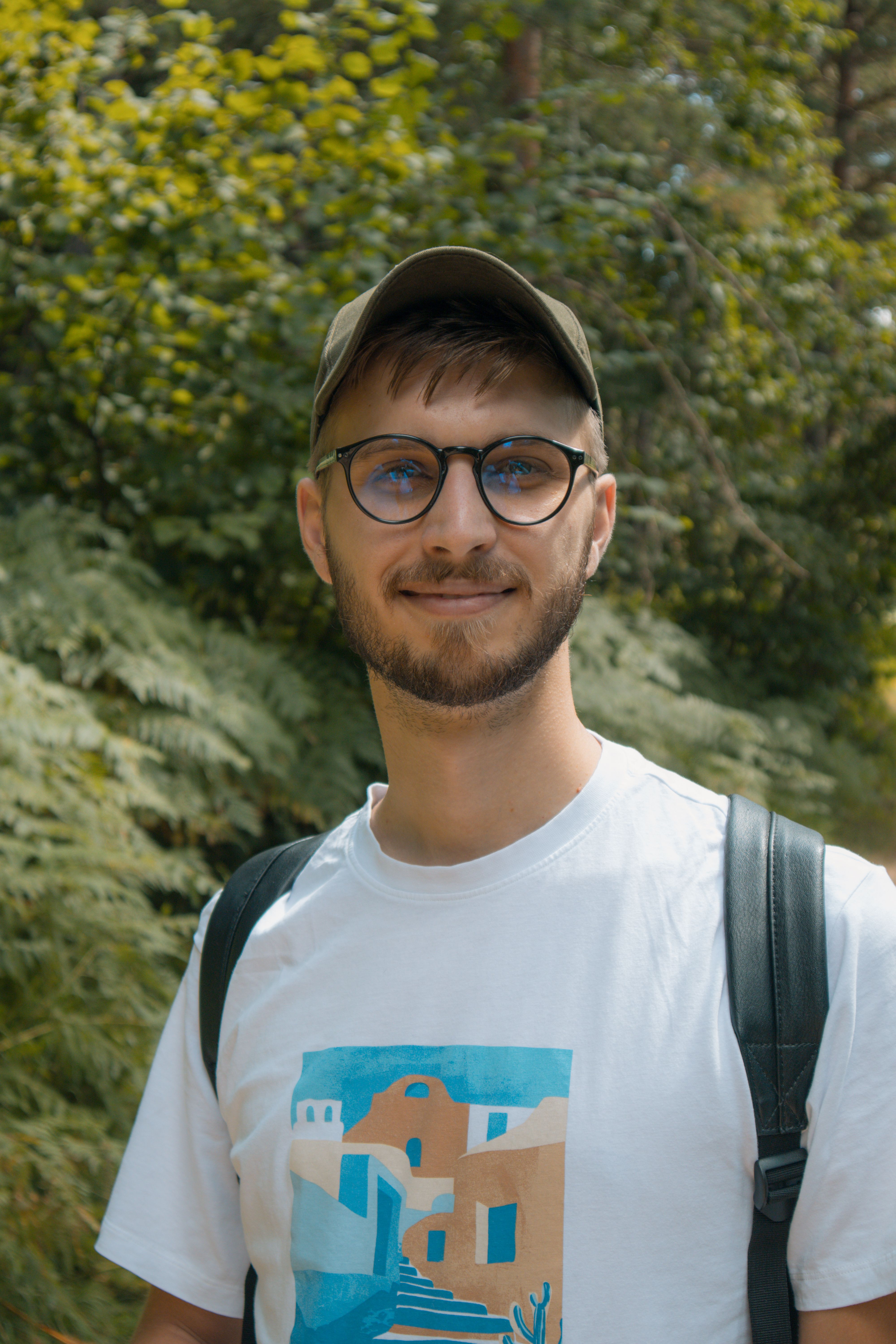Young man enjoying a walk in a lush outdoor setting, wearing a cap and glasses.