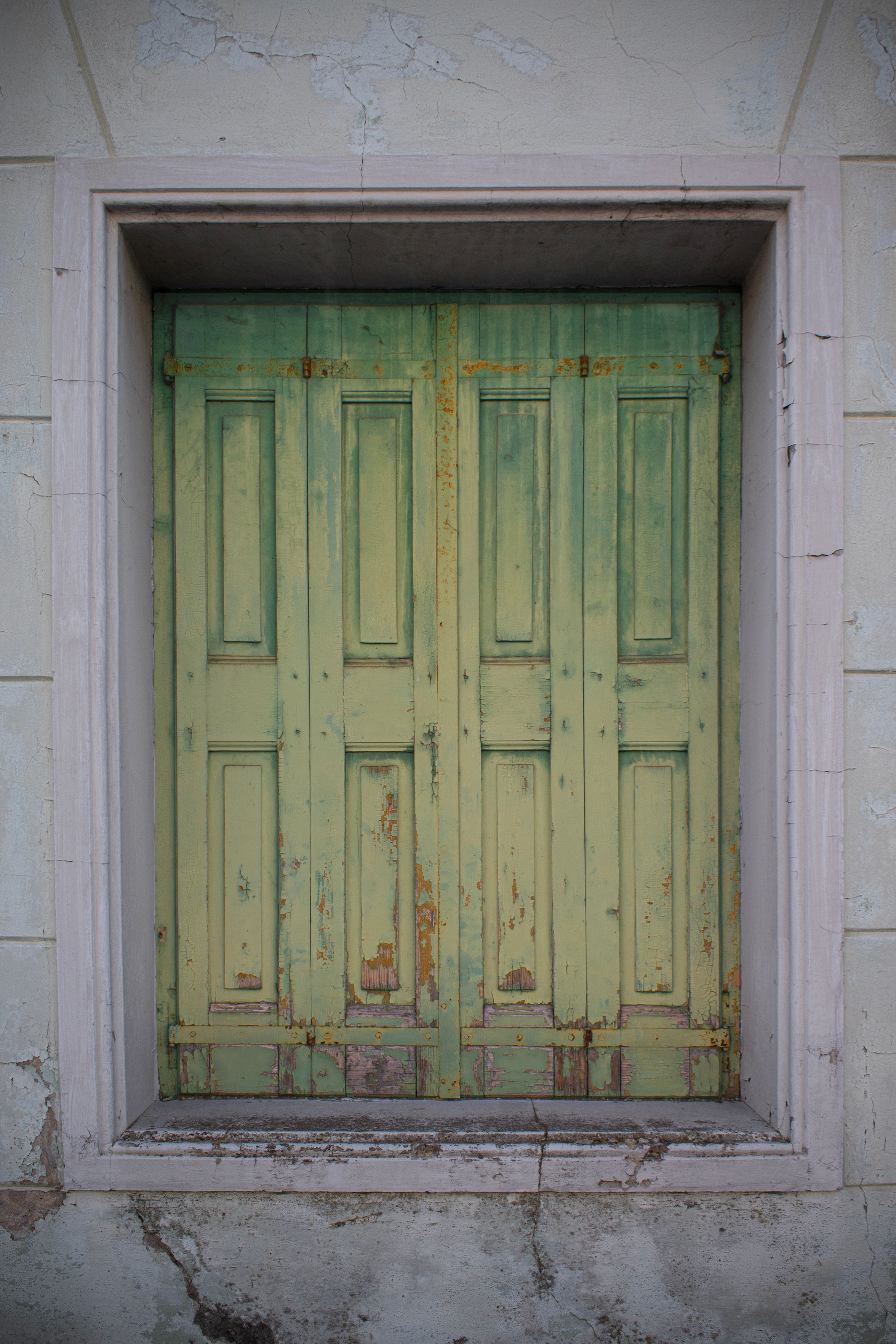 Vintage green door with peeling paint in Palmanova, Italy, showcasing rustic architecture.