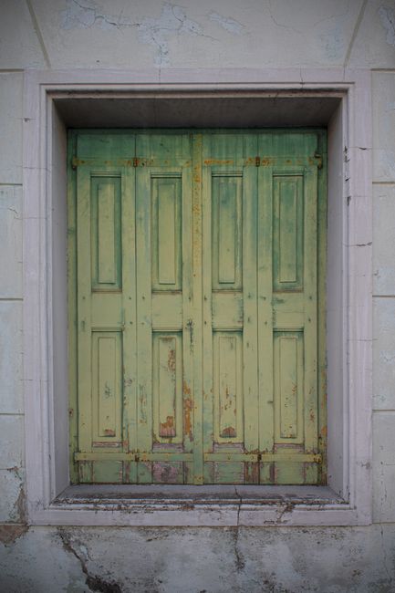 Vintage green door with peeling paint in Palmanova, Italy, showcasing rustic architecture.