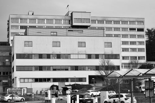 Free Black and white photo of an industrial office building facade with parked cars. Stock Photo