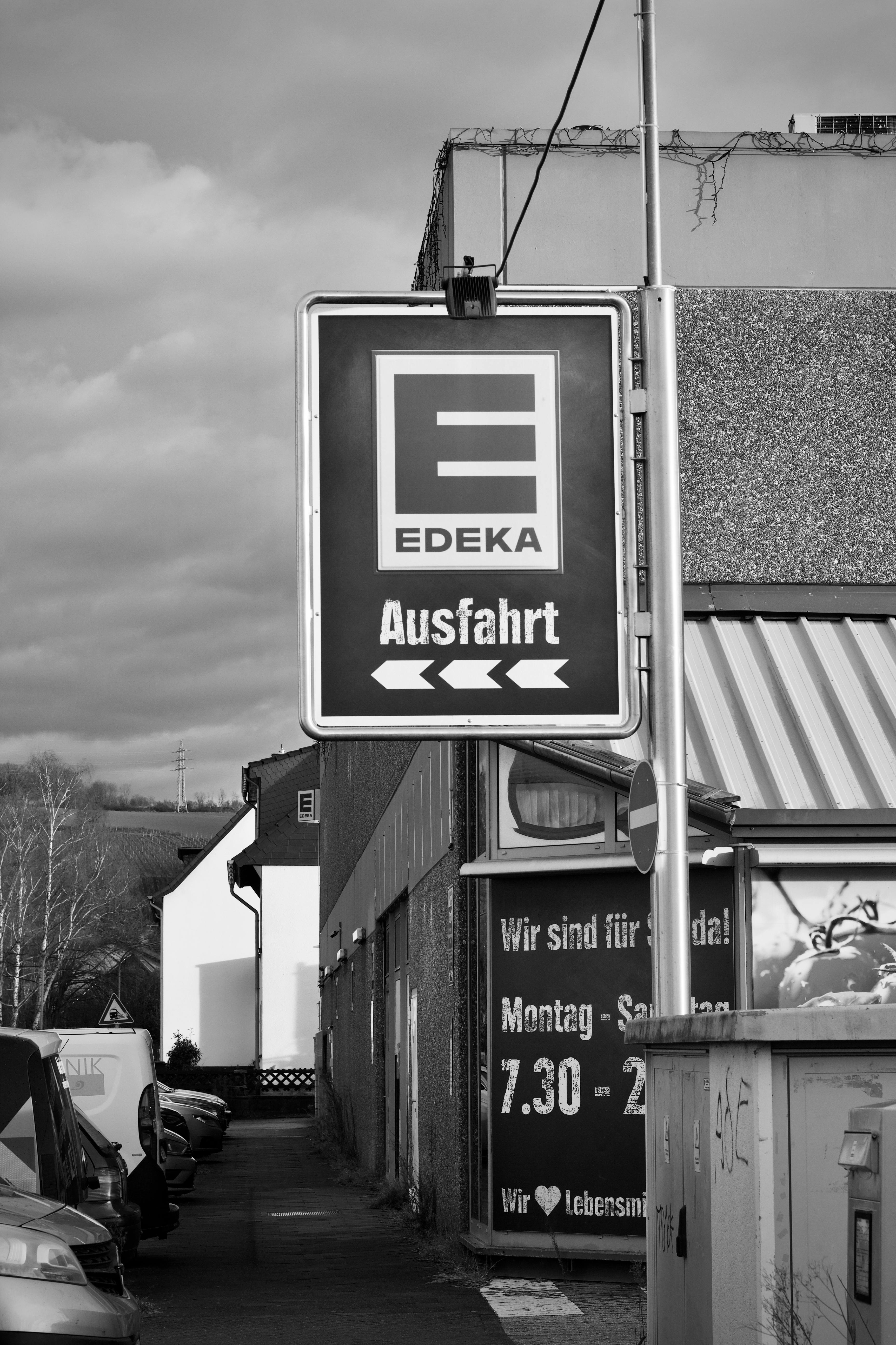 Black and white photo of an EDEKA supermarket 'Ausfahrt' sign on an urban street with cars.