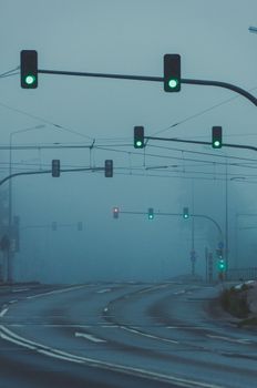 A fog-covered urban road intersection with multiple traffic lights glowing green.
