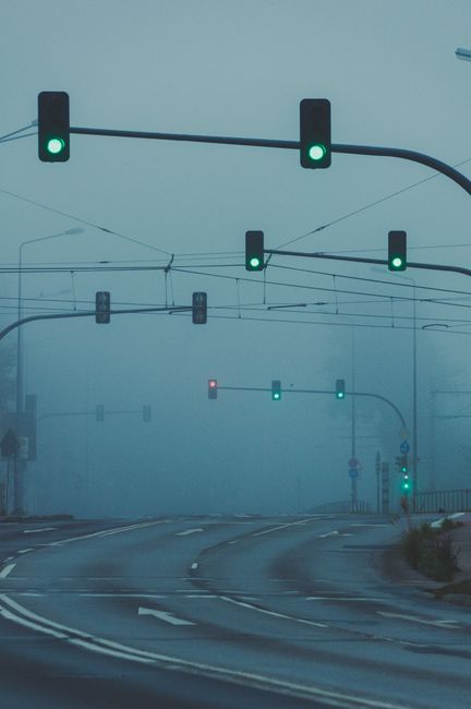A fog-covered urban road intersection with multiple traffic lights glowing green.
