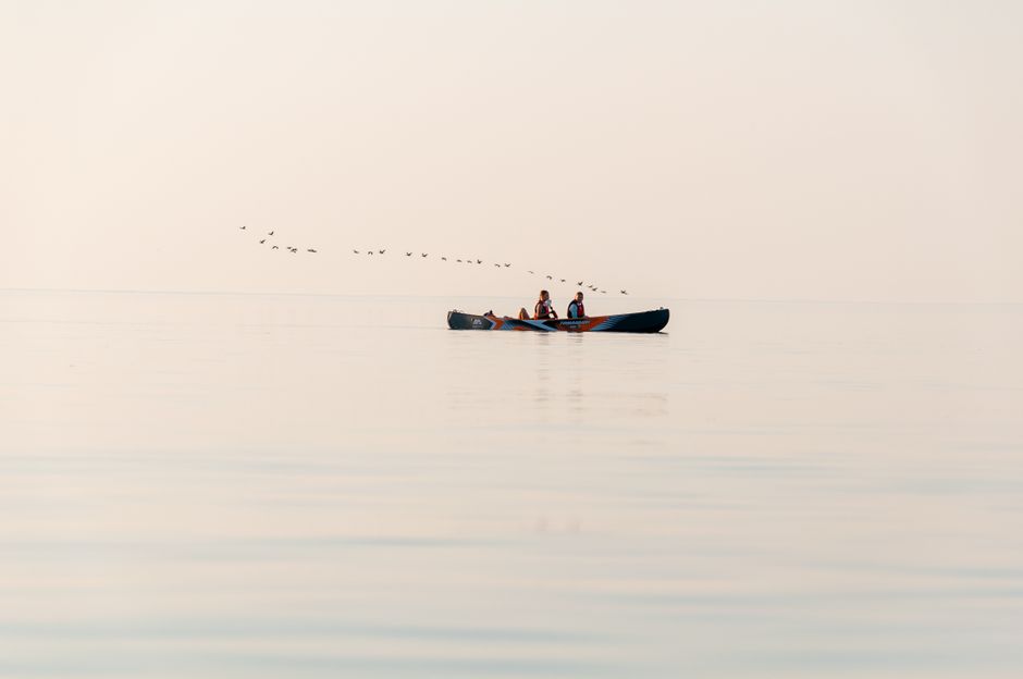 Two people enjoying a peaceful canoe ride on calm waters during sunset with birds in the sky.