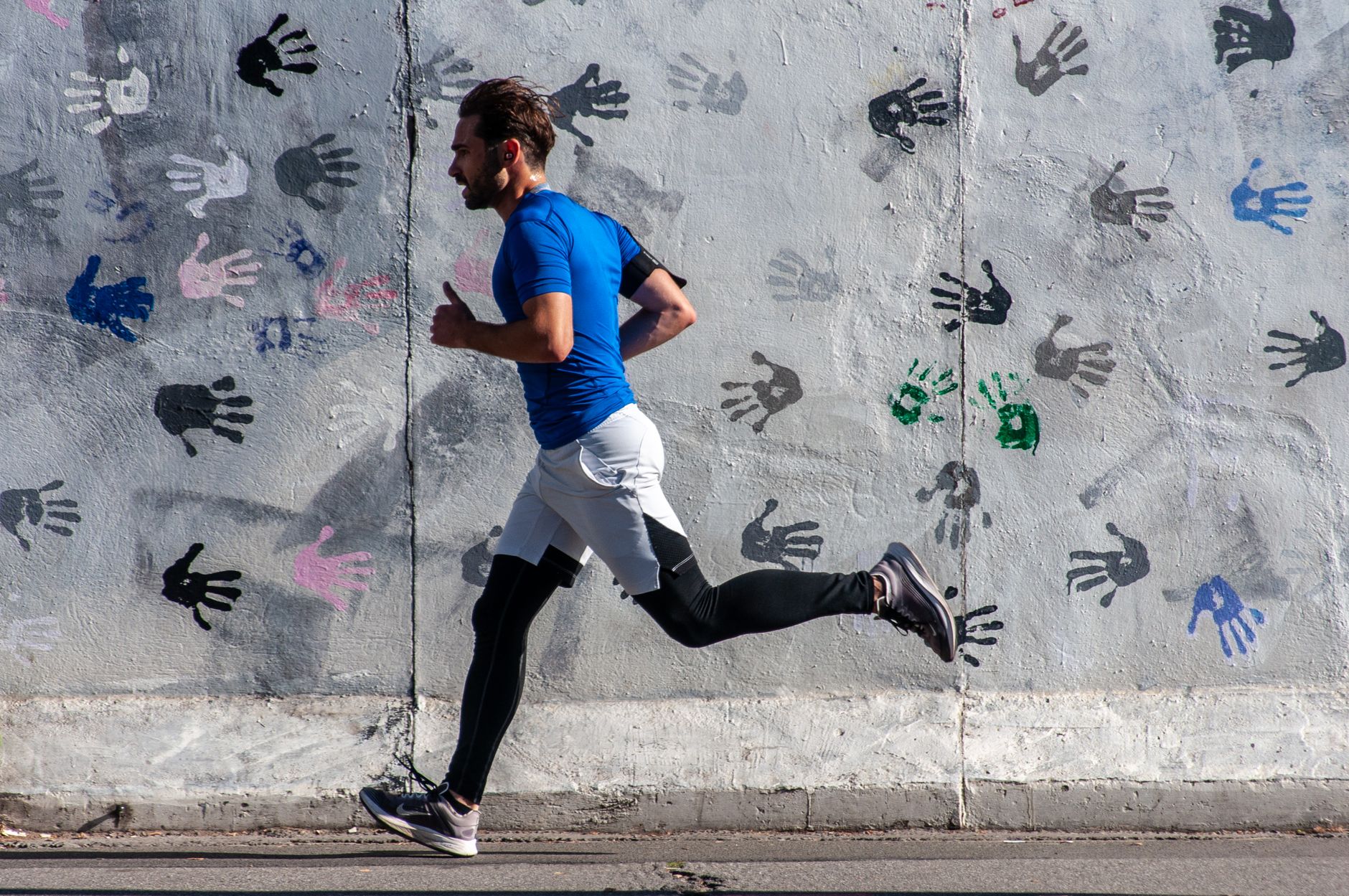 Casual jogger in sportswear runs past a colorful handprint mural, embracing urban fitness.