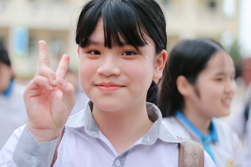 Free Young girl smiling and flashing a peace sign, wearing a school uniform outdoors. Stock Photo