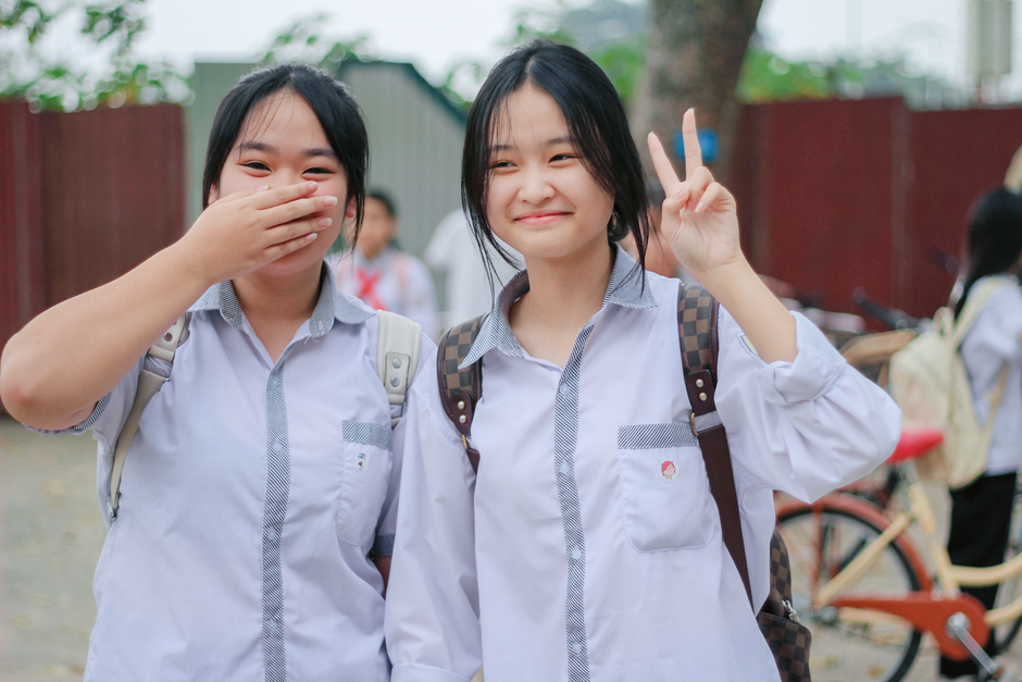 Two teenage students in uniform enjoying a lighthearted moment outside, smiling and posing with backpacks.