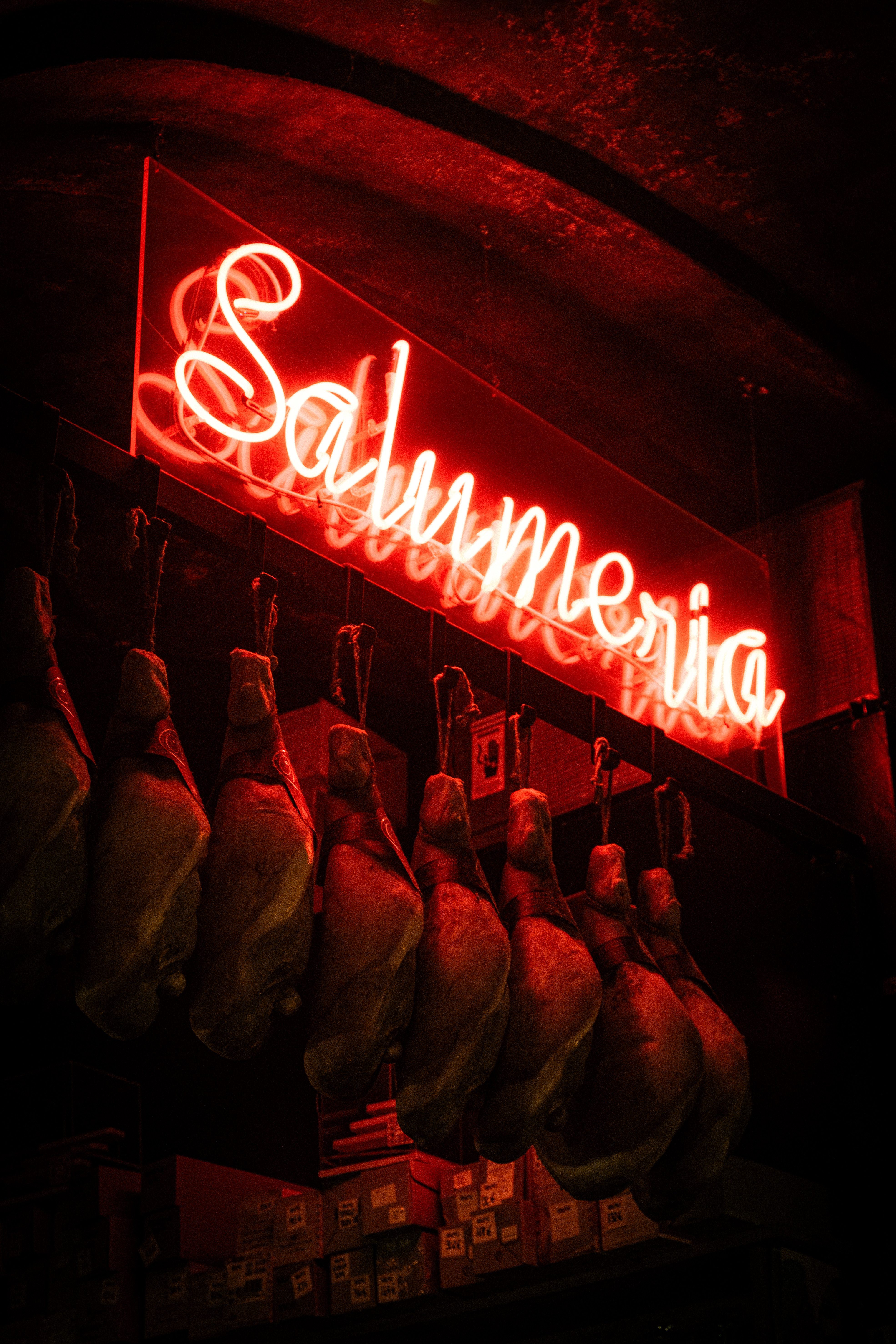 Neon salumeria sign and hanging meats in a traditional Milan deli, showcasing vibrant red lighting.