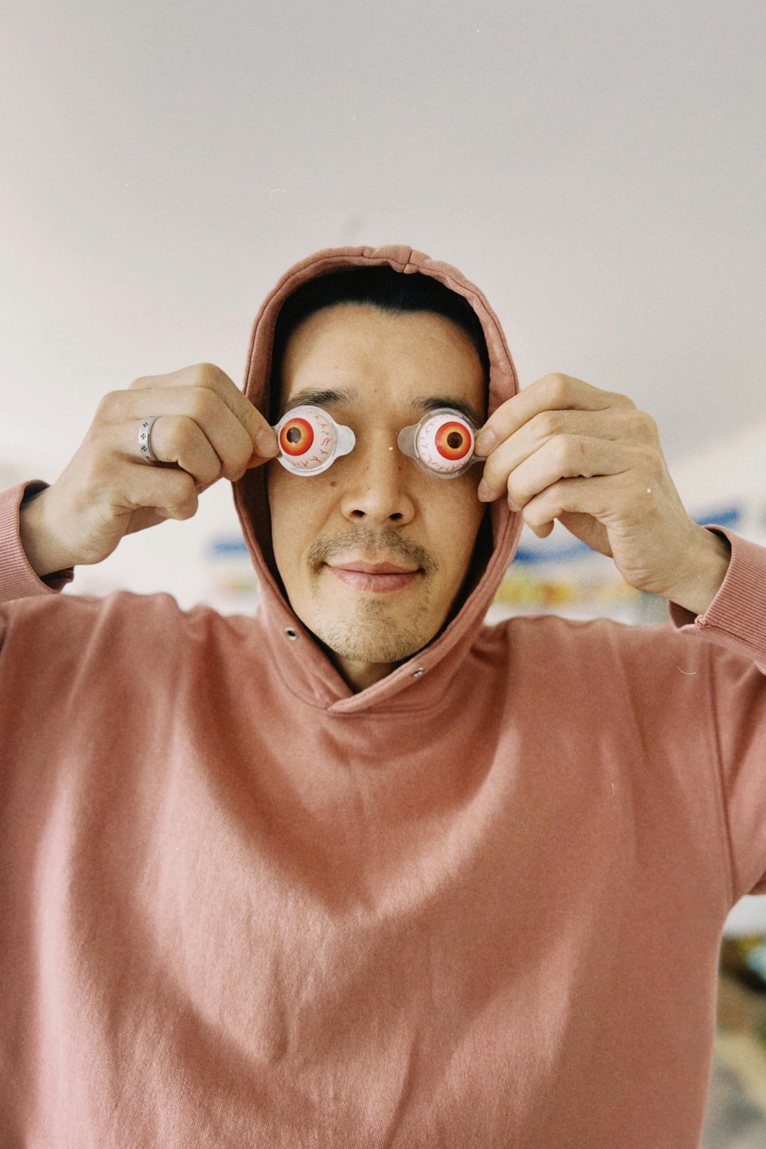 Playful portrait of an adult in a pink hoodie using candy eyeballs, creating a fun and quirky expression.