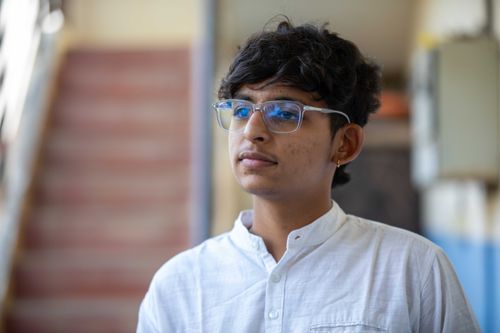 Free Portrait of a young man wearing glasses and a white shirt, looking thoughtfully indoors. Stock Photo