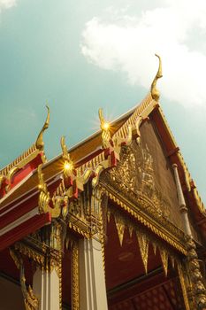 Intricate gold and red roof details of a Bangkok Buddhist temple set against a clear sky.