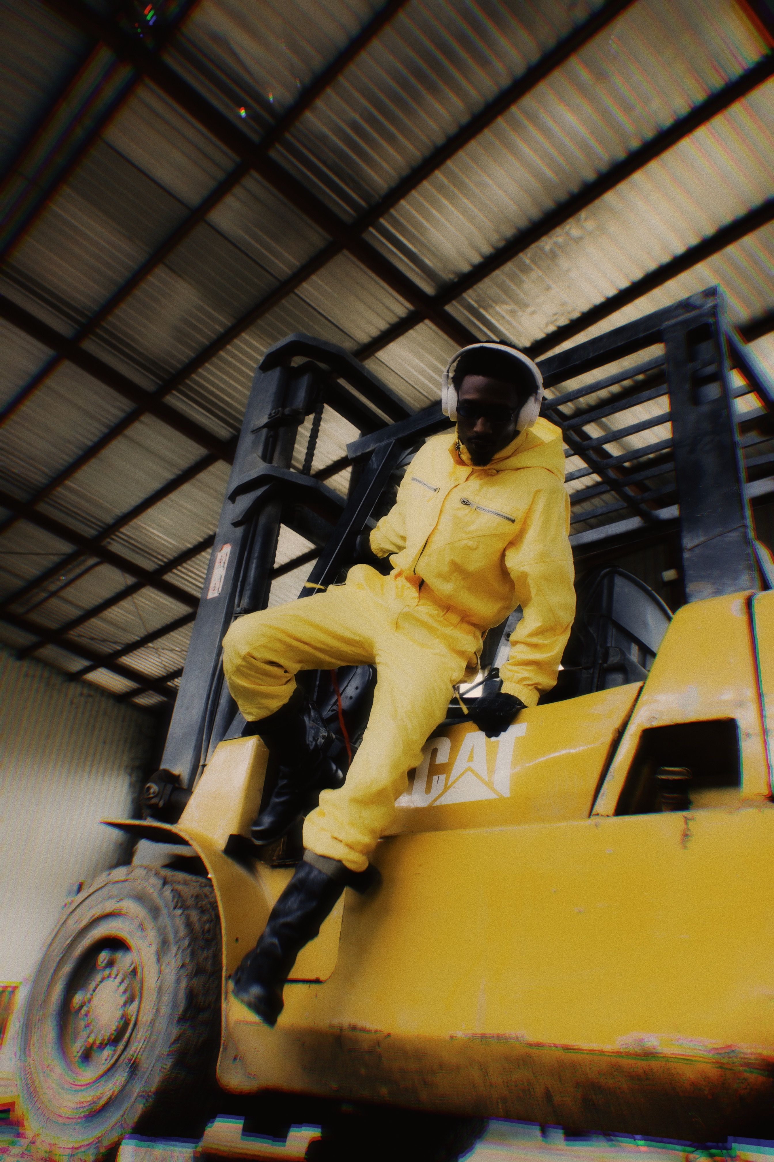 Worker in yellow safety suit operating a stand-up counterbalanced forklift in a warehouse