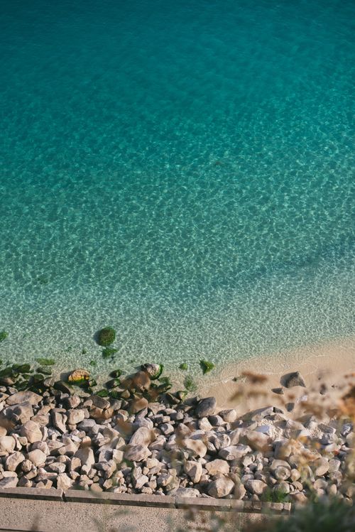 Free Serene aerial photo of a rocky beach leading into clear turquoise water, ideal for travel and nature content. Stock Photo