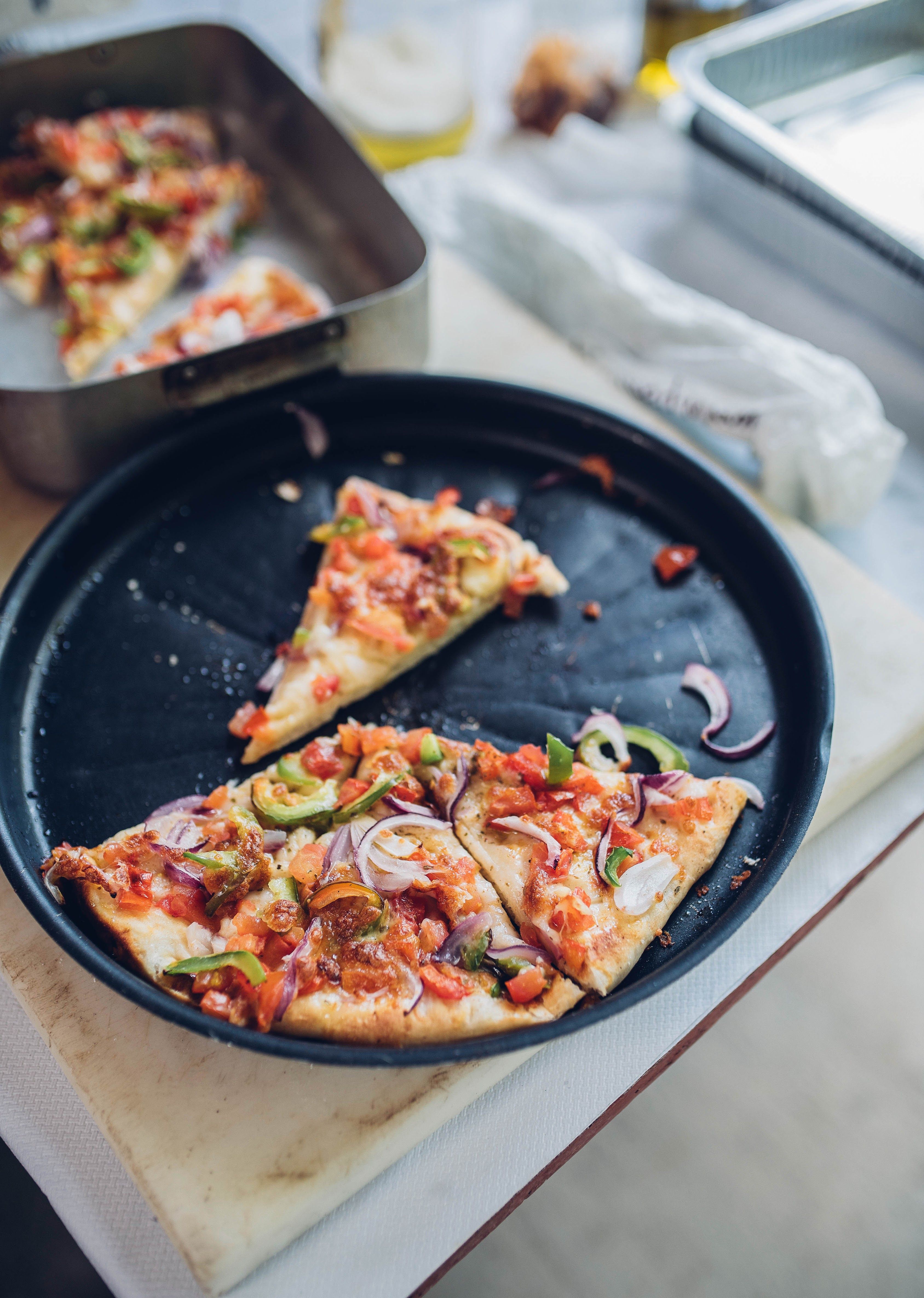 Sliced pizza in a pan surrounded by fresh toppings in a cozy kitchen setting.