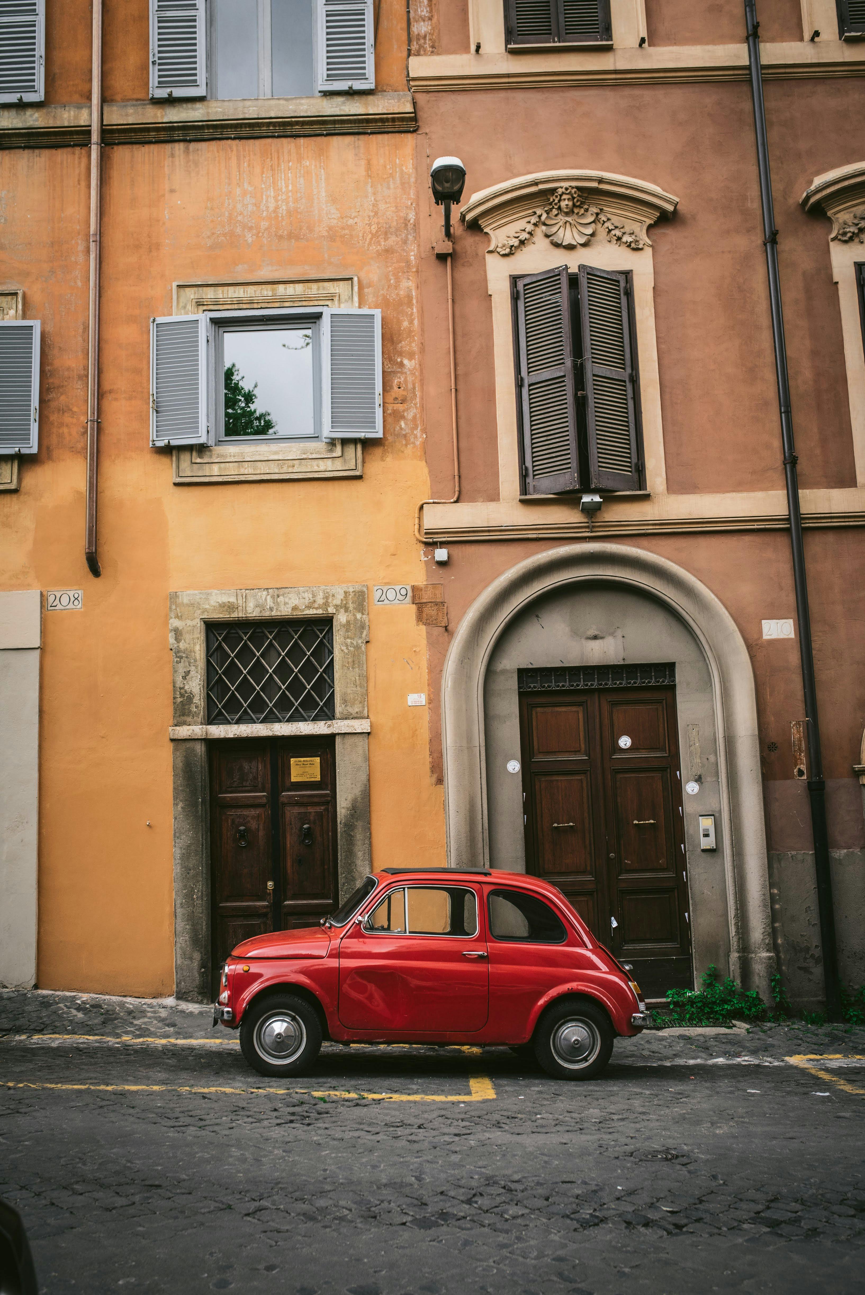 Charming red vintage car parked by an elegant historic building in a European city street.