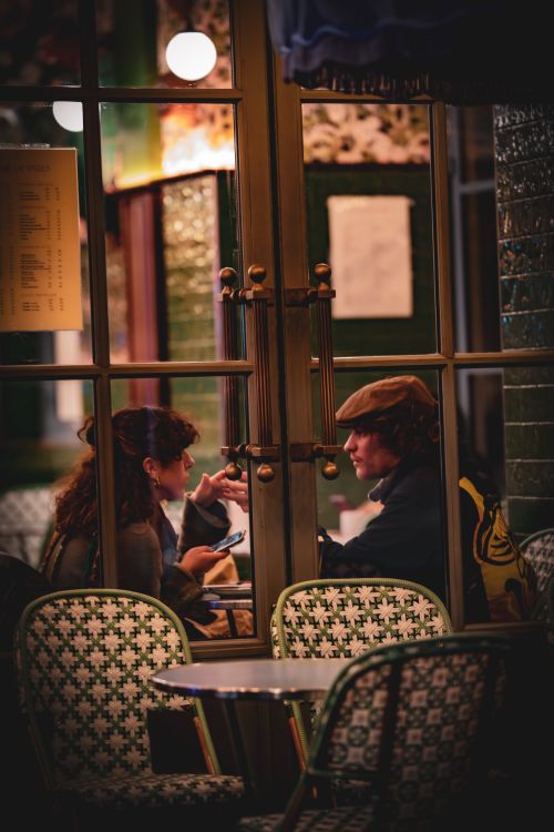 Free A couple enjoying an intimate conversation in a cozy cafe, framed by warm lighting and classic decor. Stock Photo