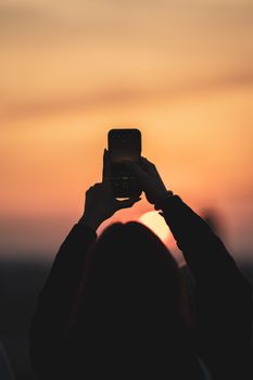 Woman silhouette capturing a stunning sunrise with a smartphone, creating a scenic composition.