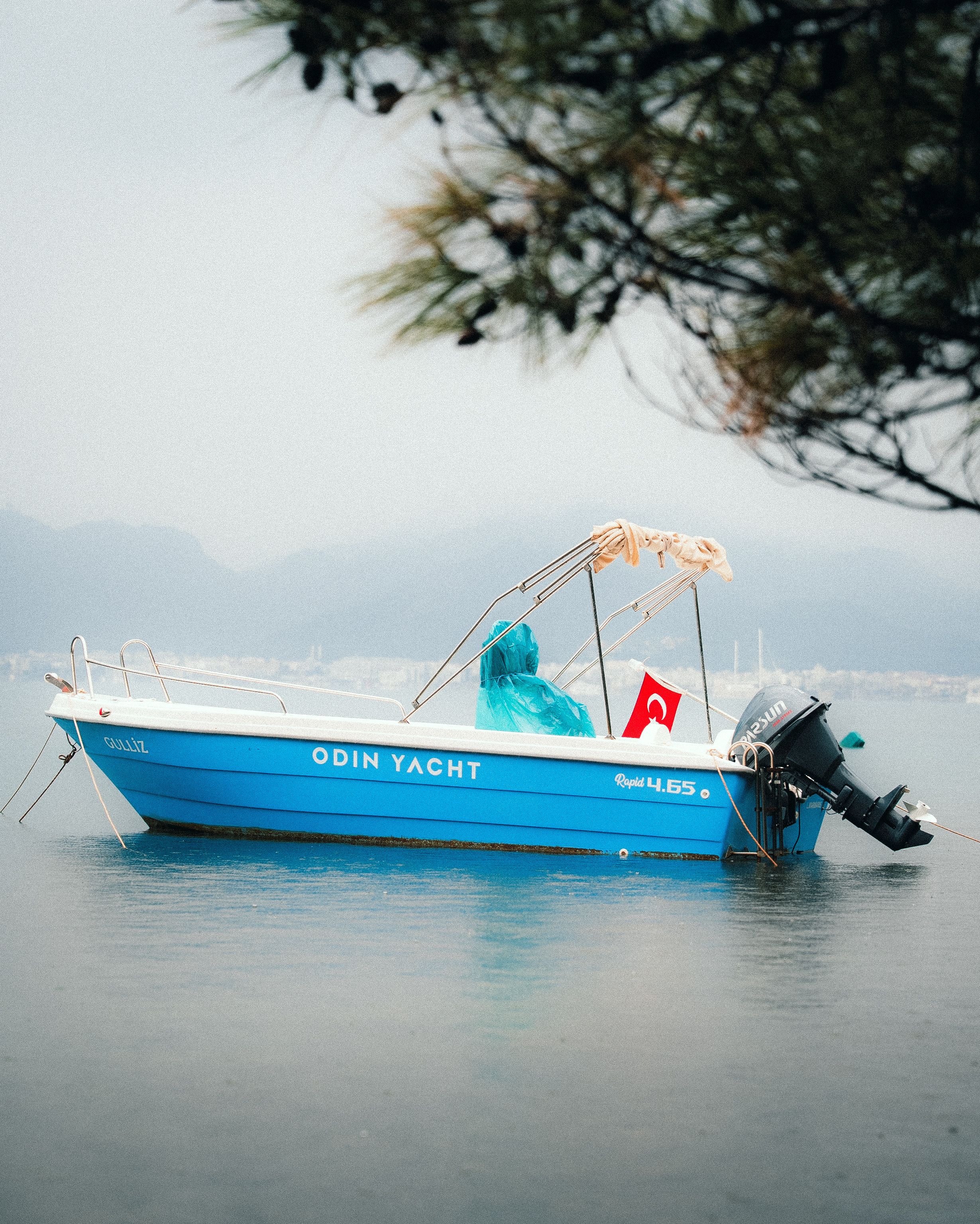 A blue yacht floats peacefully in Marmaris, Muğla, Turkey, with a Turkish flag waving gently.