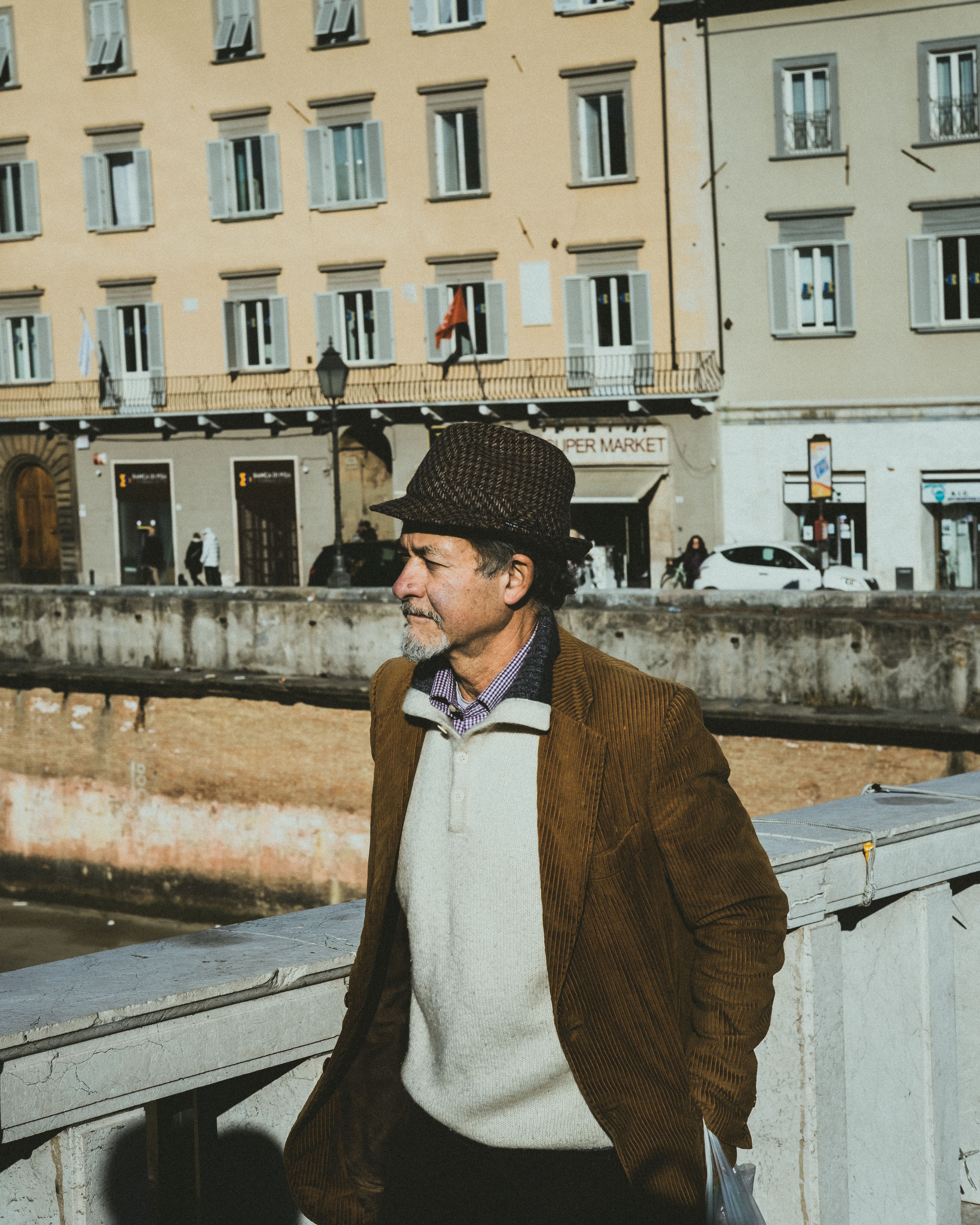 Man in vintage clothing walks on bridge in an urban setting, showcasing classic street style. Daytime, outdoor scene.
