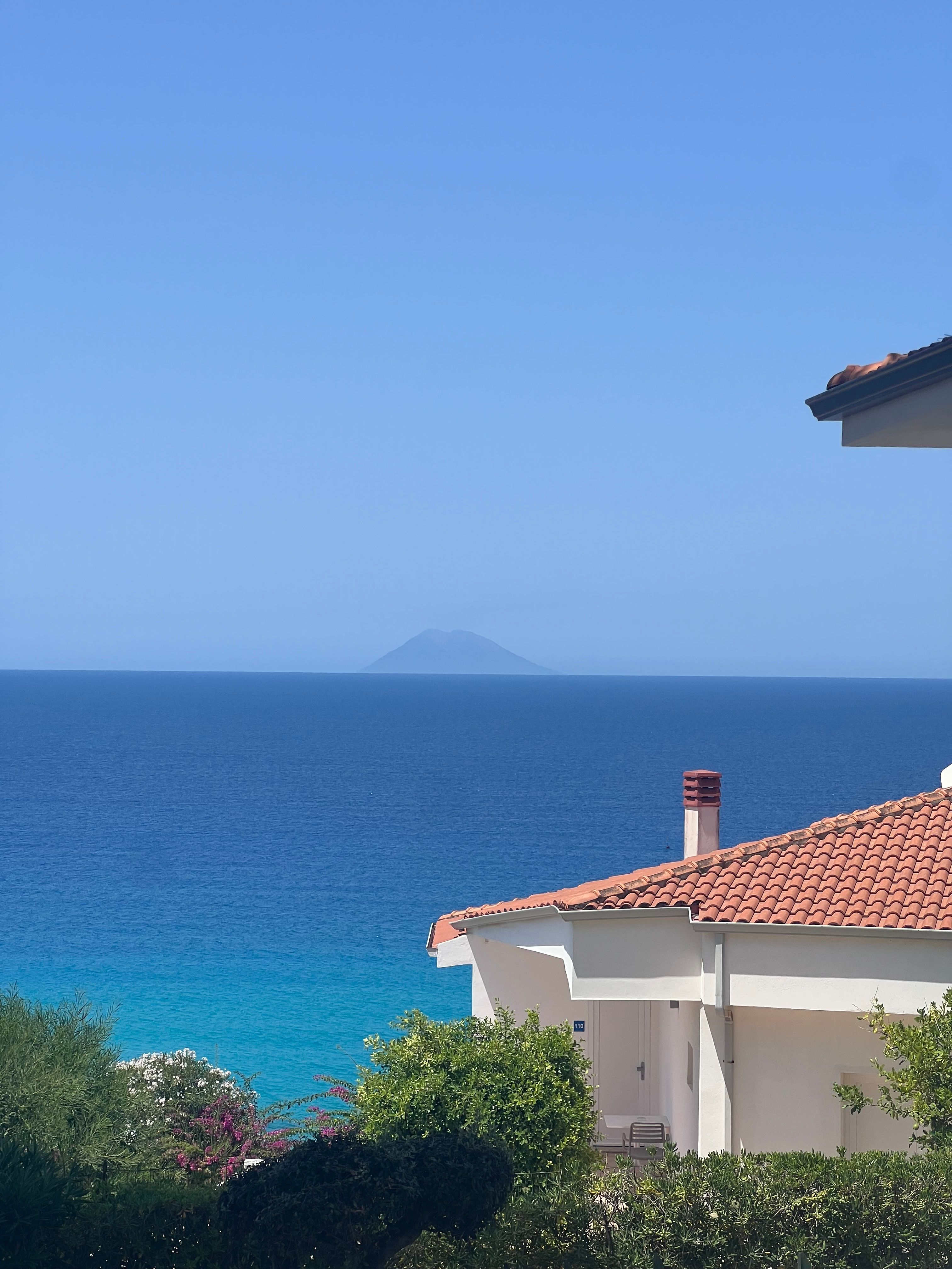 Beautiful coastal view featuring Stromboli Island in the distance with vibrant blue sea and traditional Italian roof.