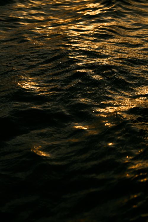 Free Close-up of ocean waves with golden sunset reflections creating a serene and magical atmosphere. Stock Photo