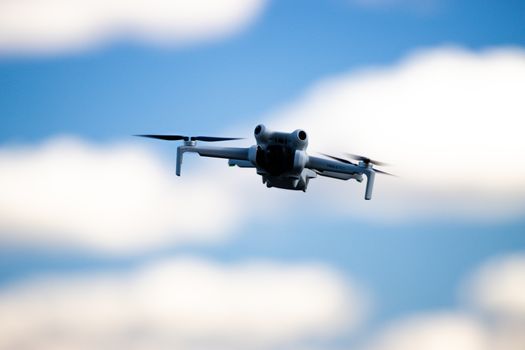 A high-tech drone soaring amidst a clear blue sky with fluffy clouds, showcasing aerial technology.