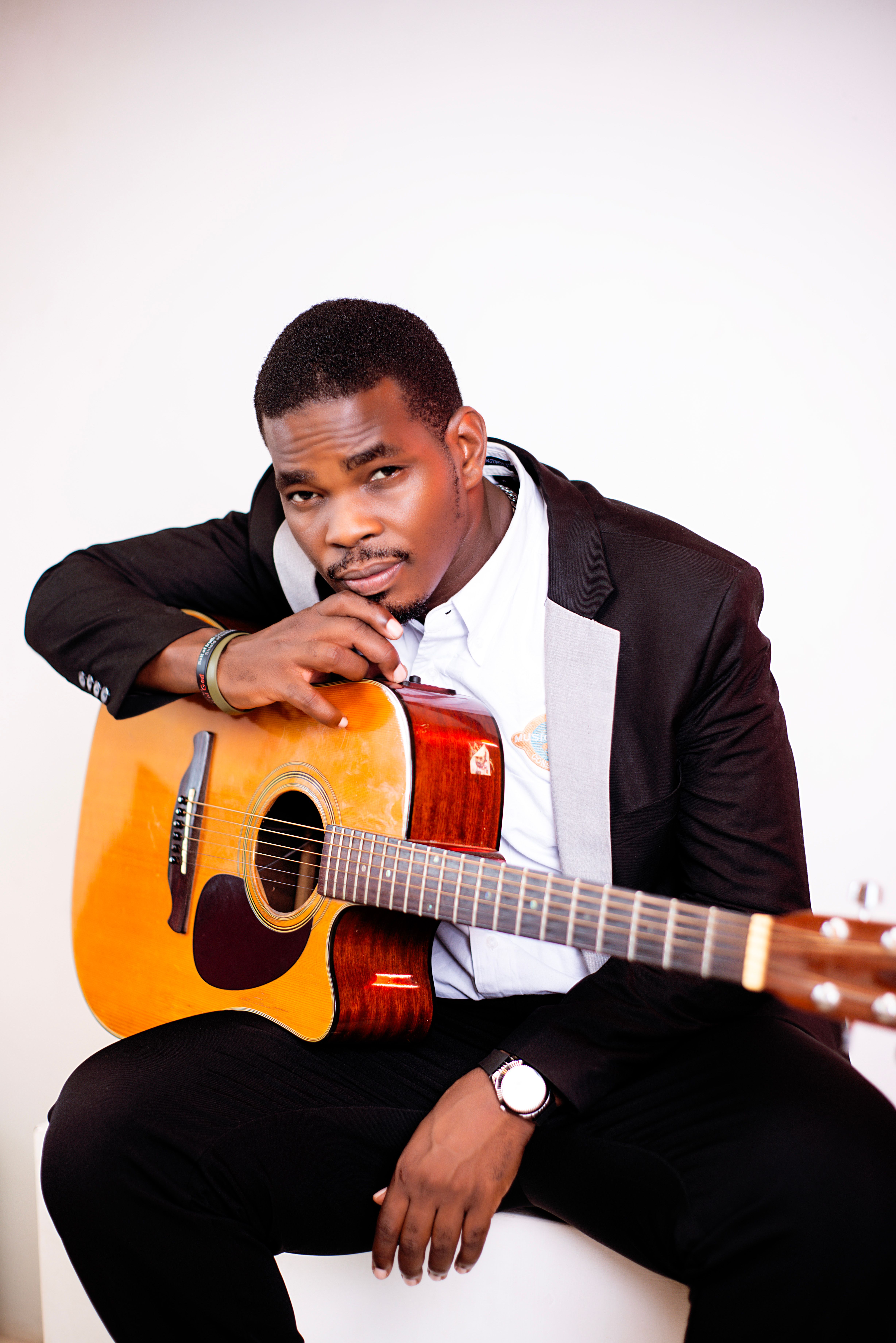Confident musician posing with an acoustic guitar, dressed in a stylish suit indoors.
