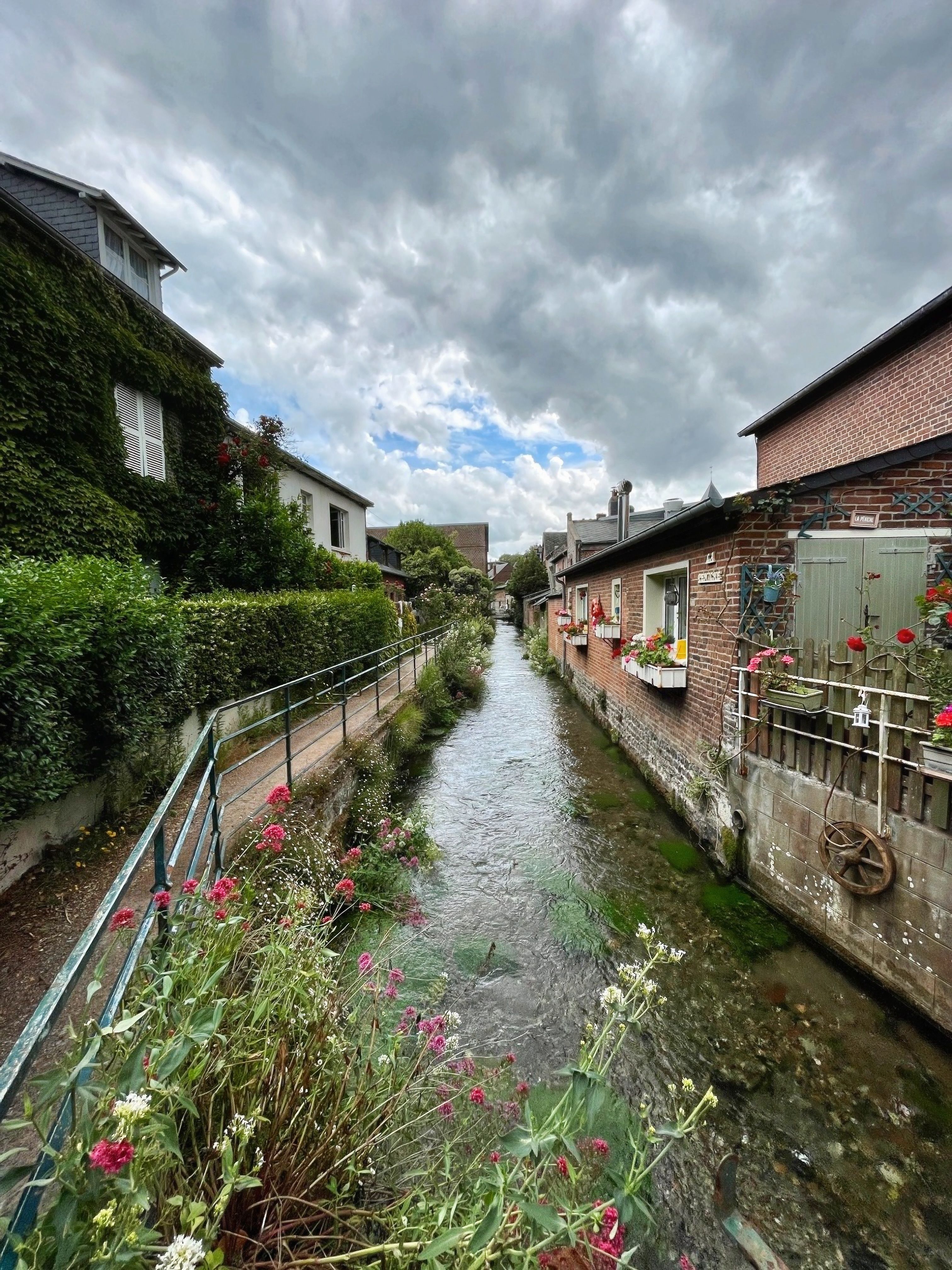 Picturesque canal view of Saint-Valery-en-Caux village in Normandie, France, with lush greenery and charming buildings.