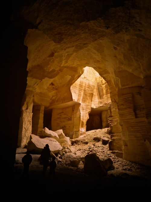 Free Silhouettes exploring a sunlit cave interior with dramatic rock formations. Stock Photo