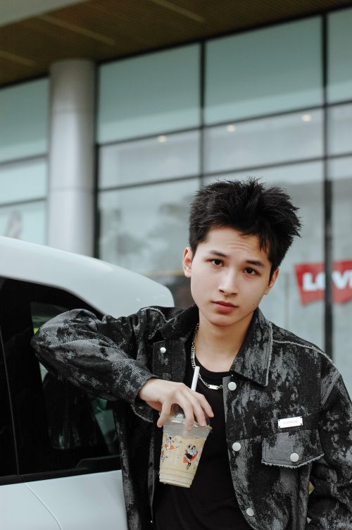 Free Casual young man leaning on a car, holding iced coffee, outdoors. Stock Photo