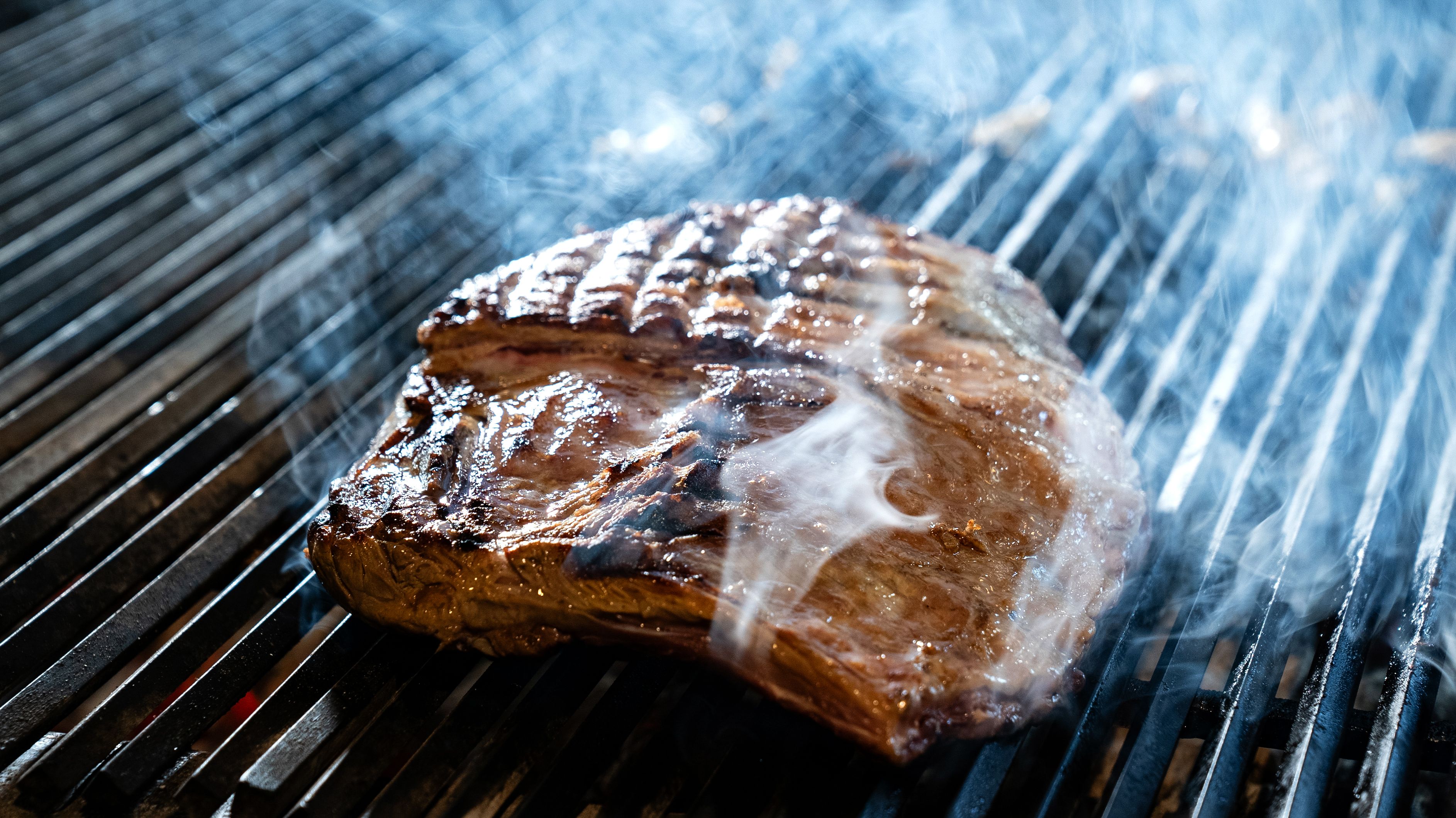 Grilled coulotte steak sizzling on the grill with herbs