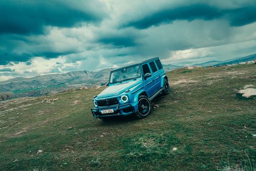 Free A blue Mercedes G Wagon parked on a rugged mountainside under a dramatic cloudy sky. Stock Photo