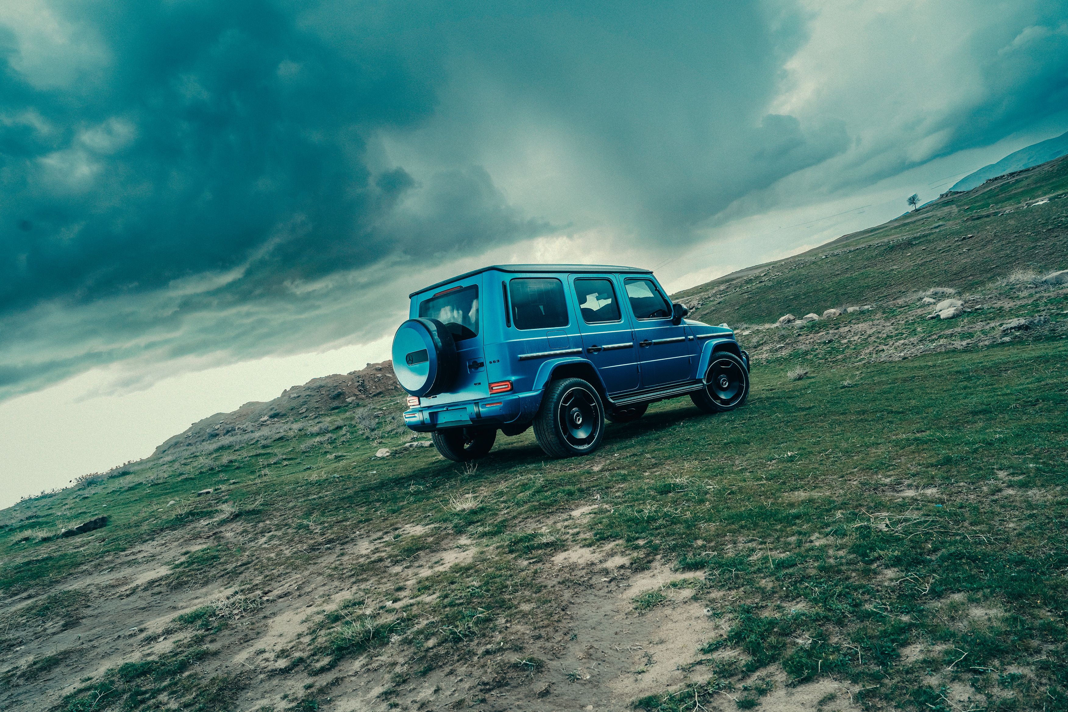 Blue SUV parked on a rugged terrain with dramatic clouds, showcasing adventure and off-road capability.