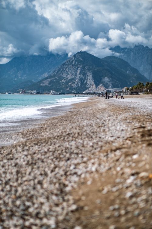Free Scenic view of a pebble beach against a mountainous landscape under a cloudy sky. Stock Photo