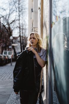 Stylish young woman in black attire leaning against a wall in a city street, expressing modern street fashion.