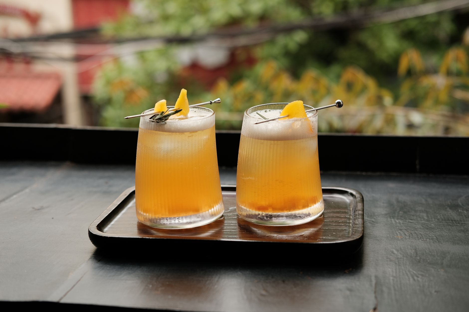 Two refreshing orange cocktails with garnish on a dark tray outdoors.
