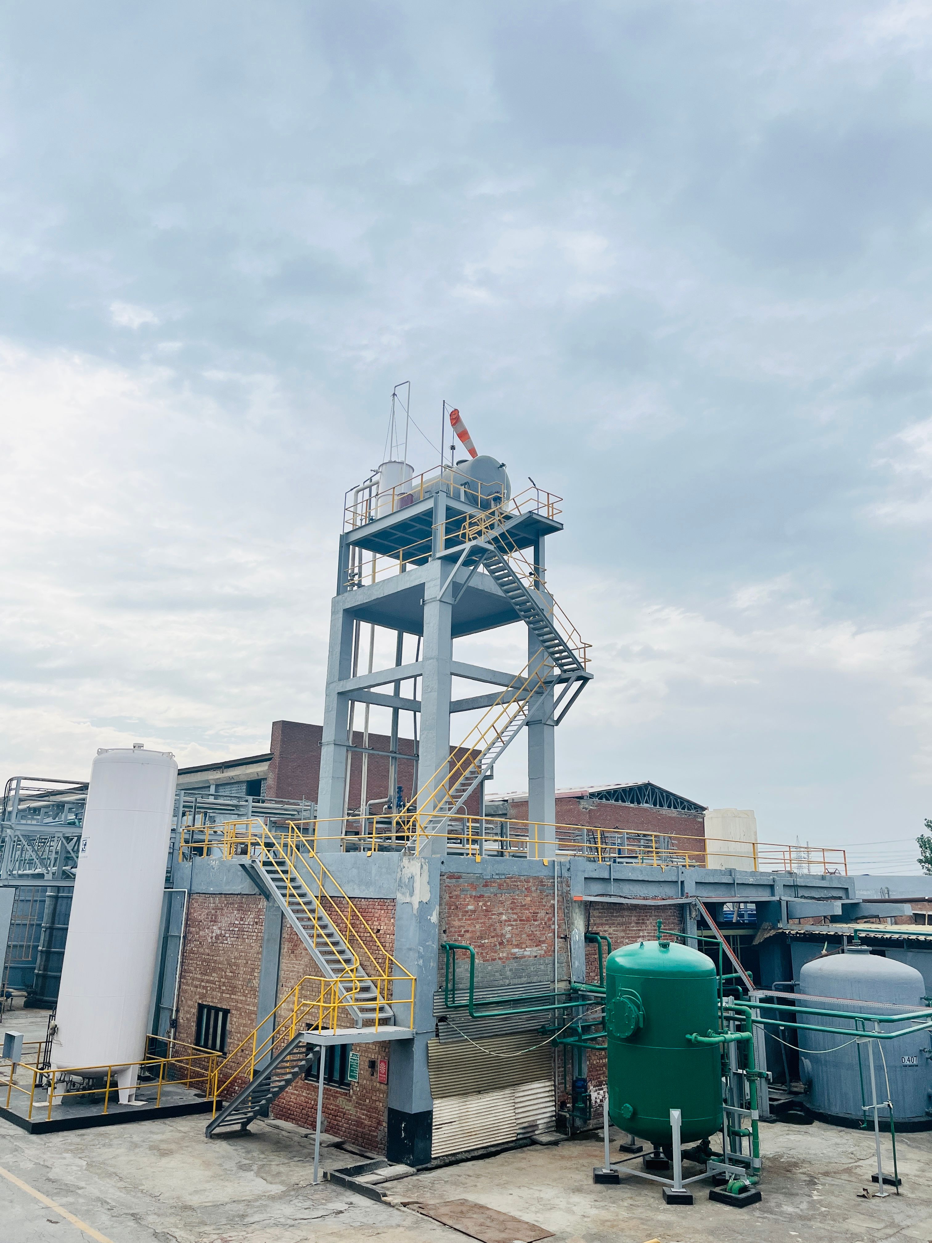 Exterior view of an industrial facility with machinery and tanks under a cloudy sky, showcasing manufacturing infrastructure.