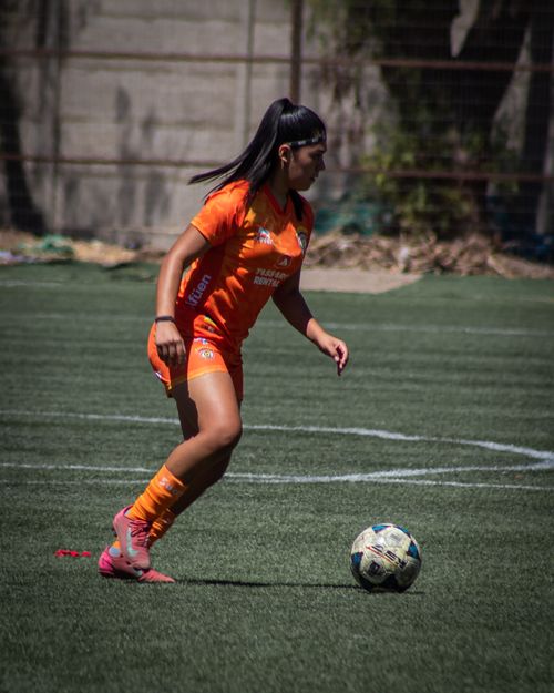 Free A female soccer player in orange uniform dribbling a ball on a sunny day. Stock Photo