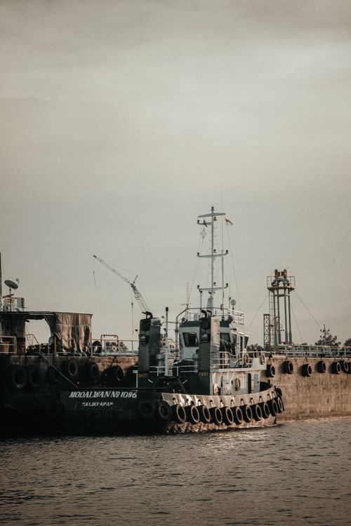 Free Tugboat beside a large ship at a bustling maritime industrial port during daytime. Stock Photo