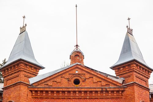 Free Red brick building with two pointed metal towers featuring intricate designs on a cloudy day. Stock Photo
