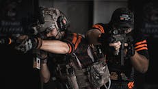 两名武装人员穿着战术装备，正在进行逼真的室内战斗训练