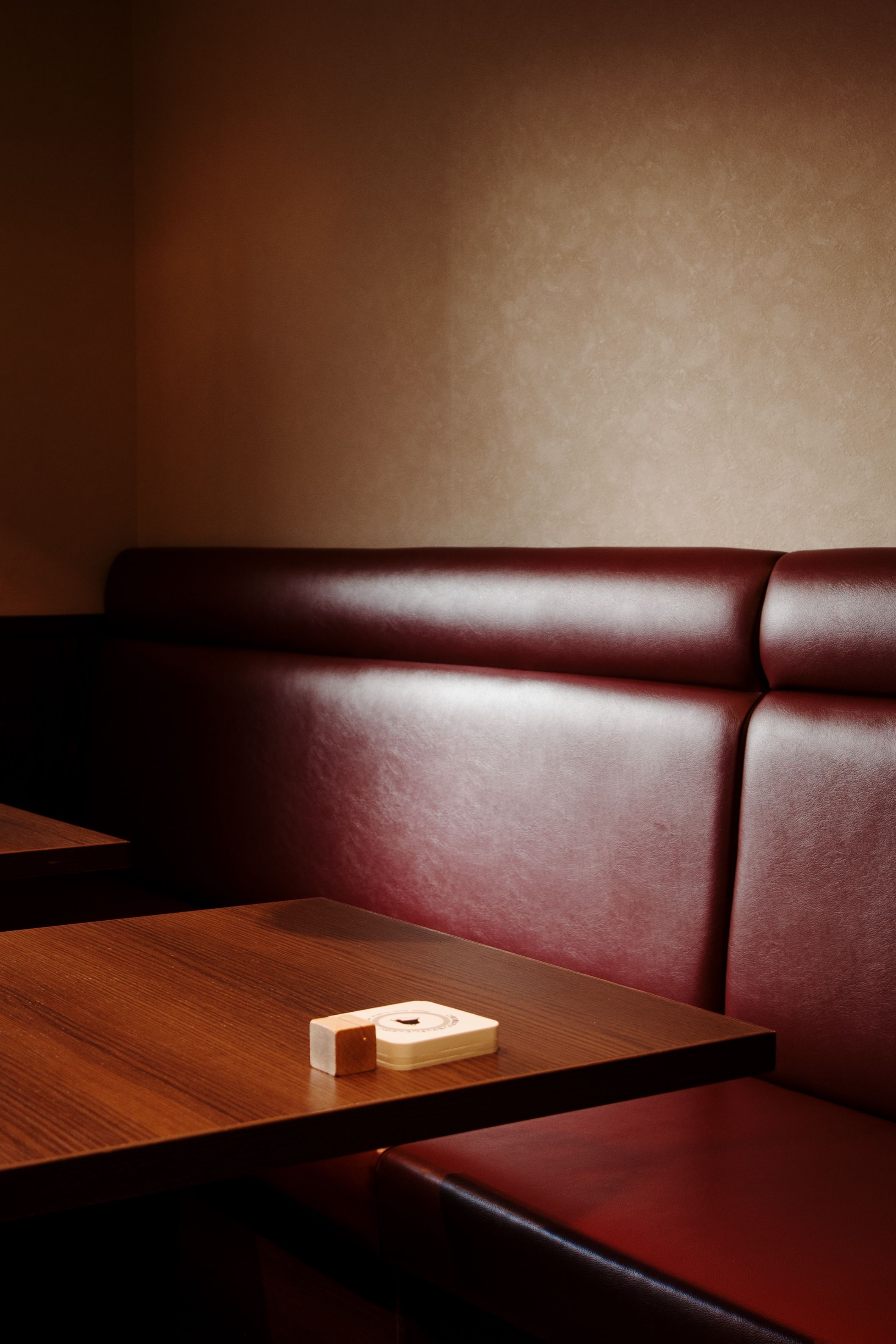 Coin de salle de restaurant : banquette en cuir bordeaux et table en bois sous une lumière douce