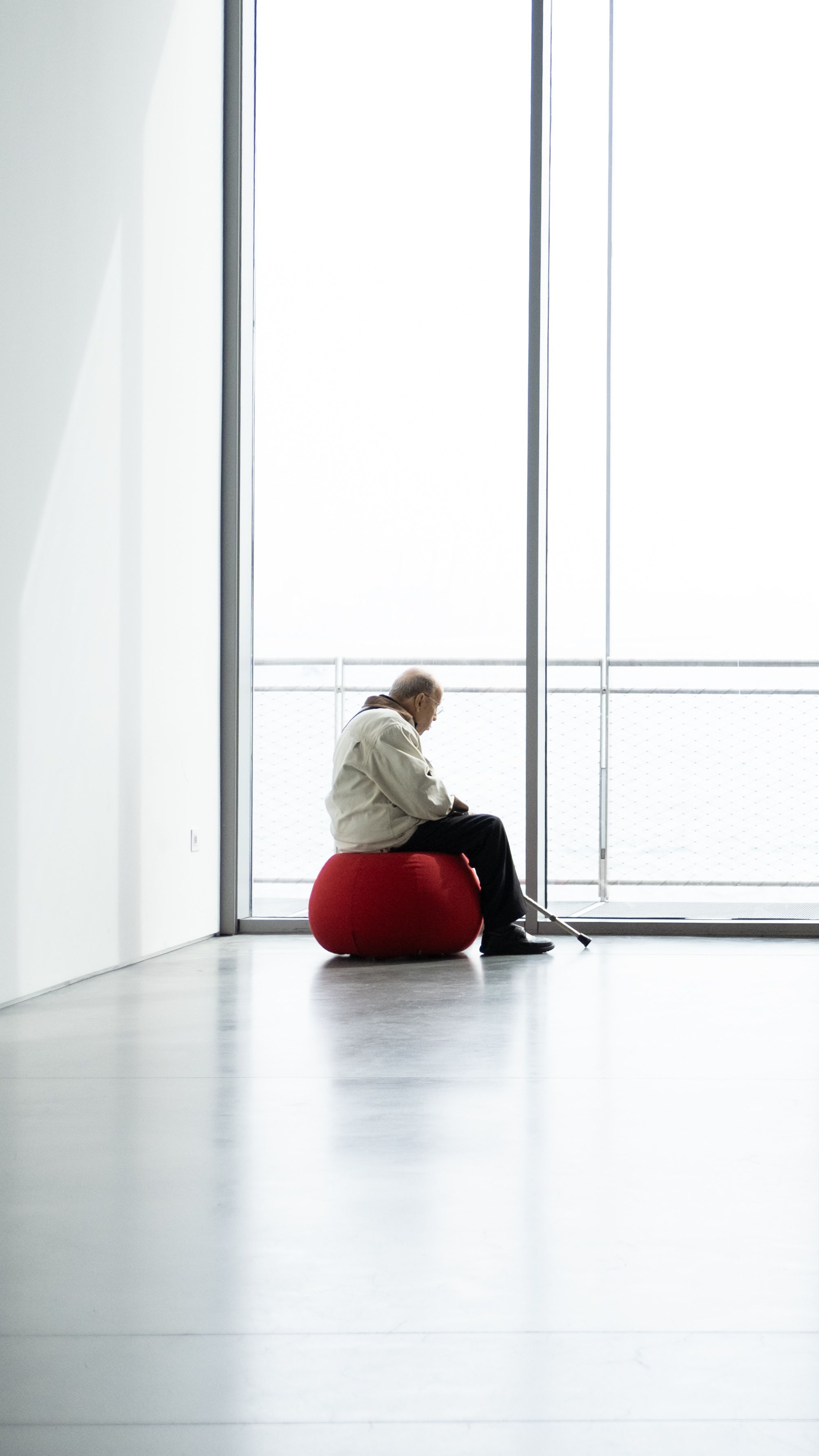 A person sits alone on a red chair in a minimalist interior, gazing outside.