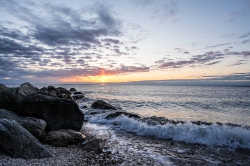 Free Serene sunset view with waves crashing on a rocky beach, capturing tranquil ocean vibes. Stock Photo