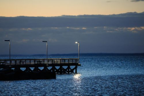 Free Serene twilight view of a pier extending into the ocean, with gentle reflections on the water. Stock Photo