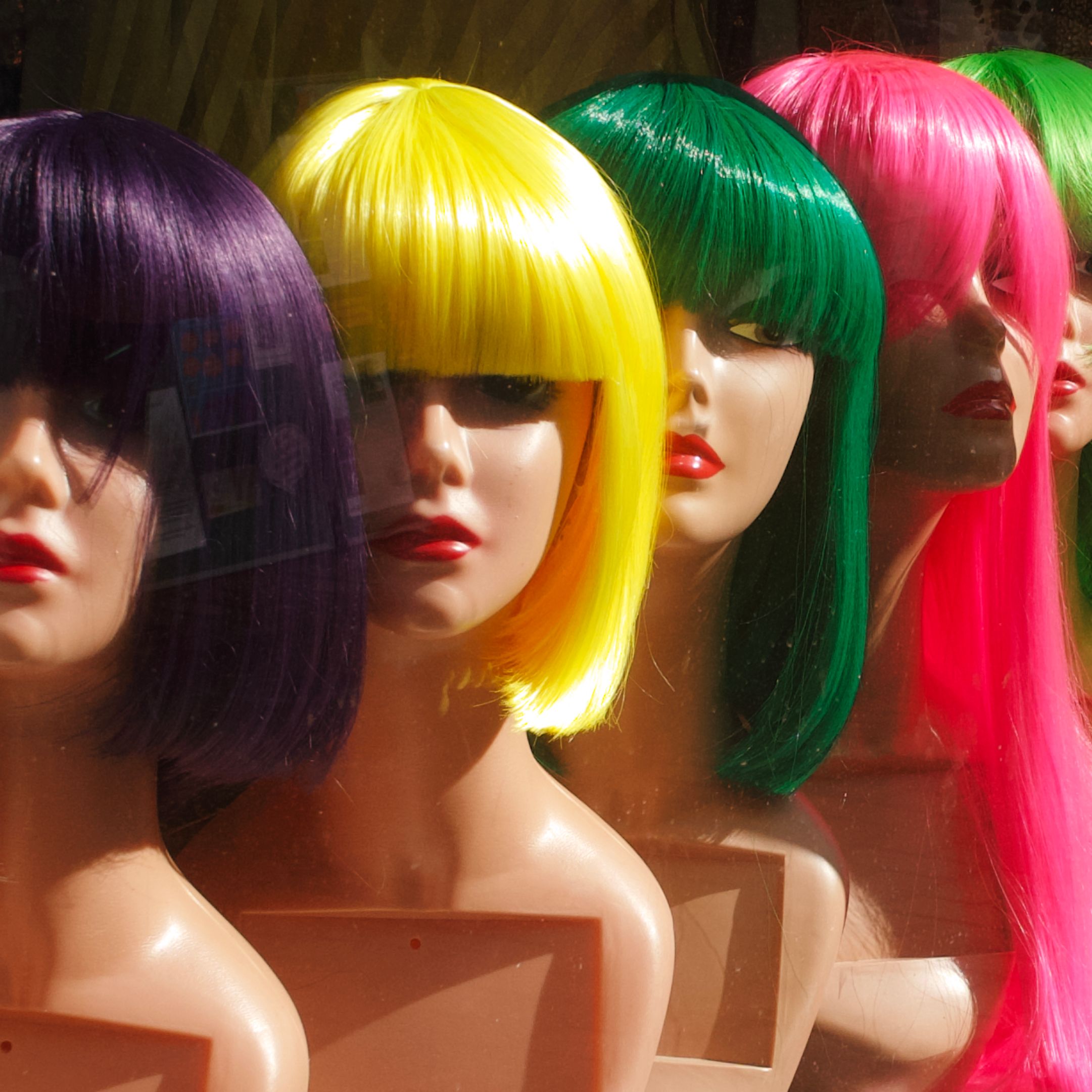 Vibrant wigs on mannequin heads showcasing bright colors in a storefront display.