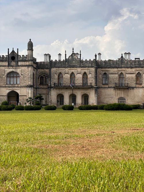 Free A picturesque view of a historic castle with Gothic architecture, surrounded by lush greenery under a cloudy sky. Stock Photo