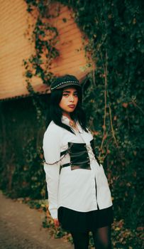 A young woman confidently poses in a stylish black and white outfit against a leafy background.