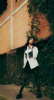 Young woman in white shirt and skirt posing confidently against ivy-covered brick wall.